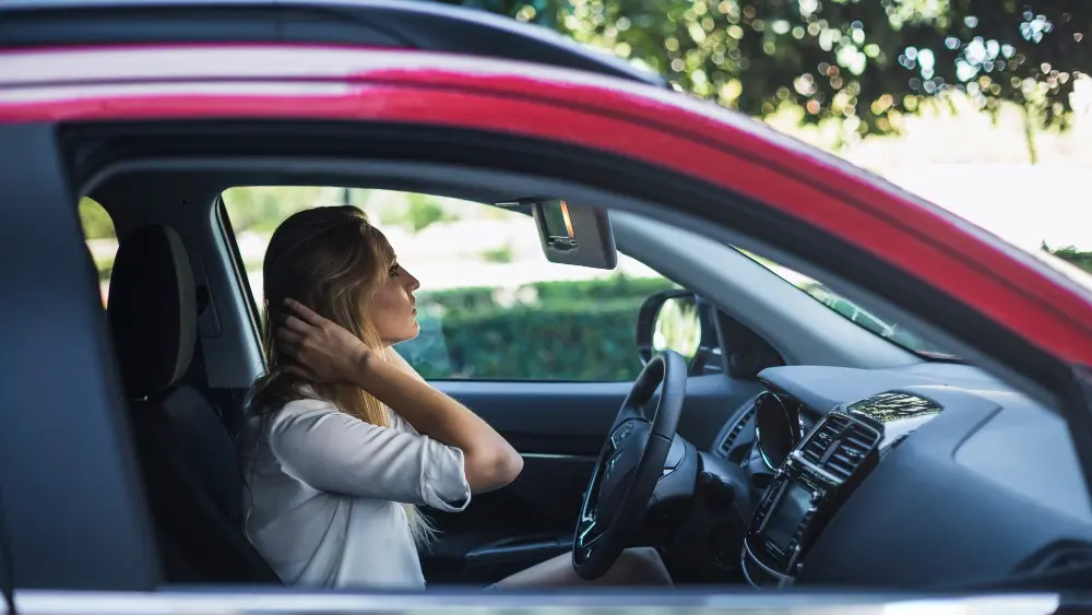 Woman in car holding neck due to whiplash injury after accident