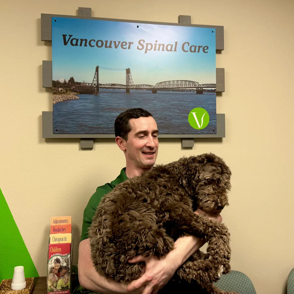 Dr. Scott Freeman sitting under Vancouver Spinal Care sign holding office dog Mia